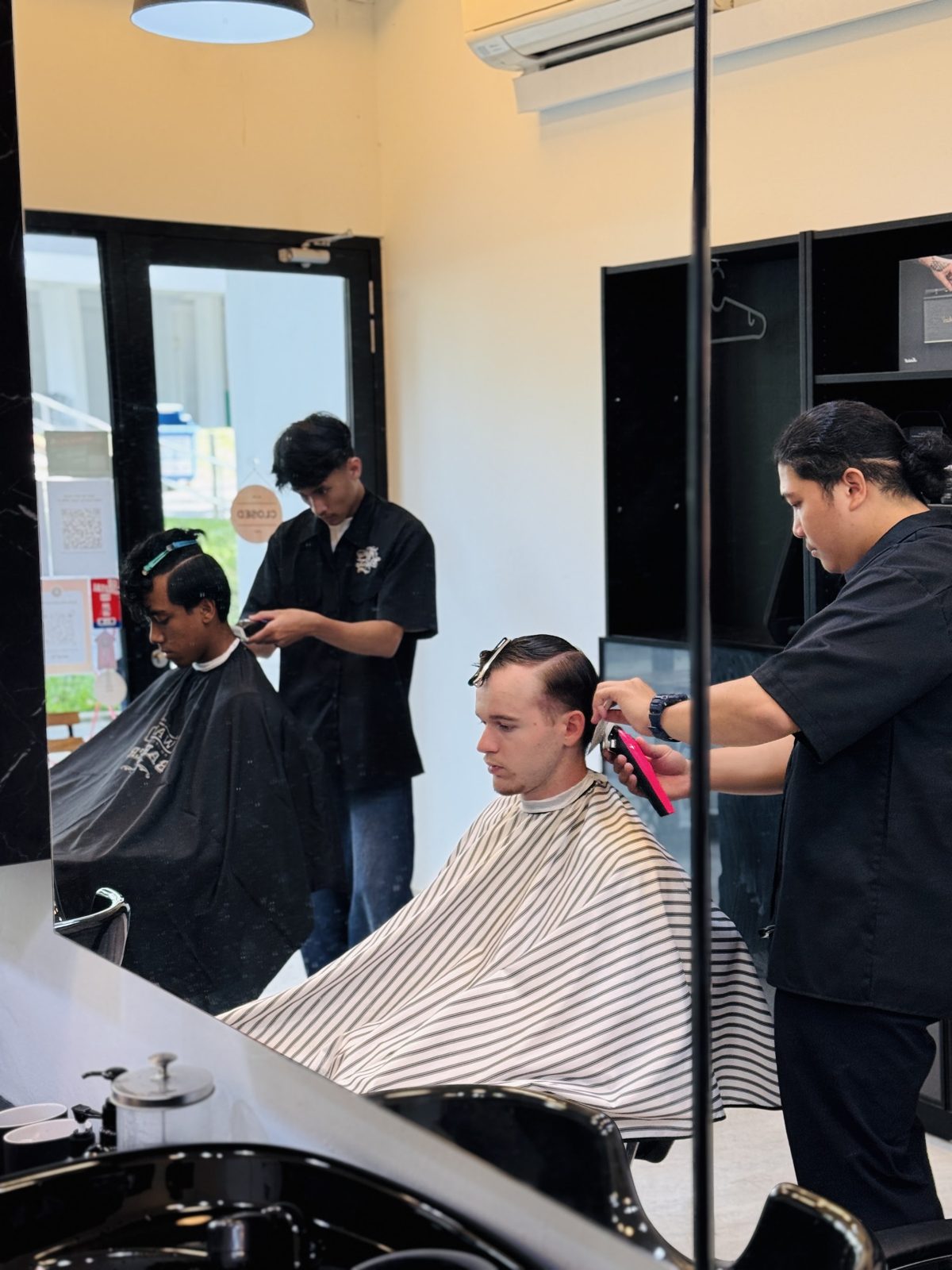 Two barbers working in a bright mirrored shop